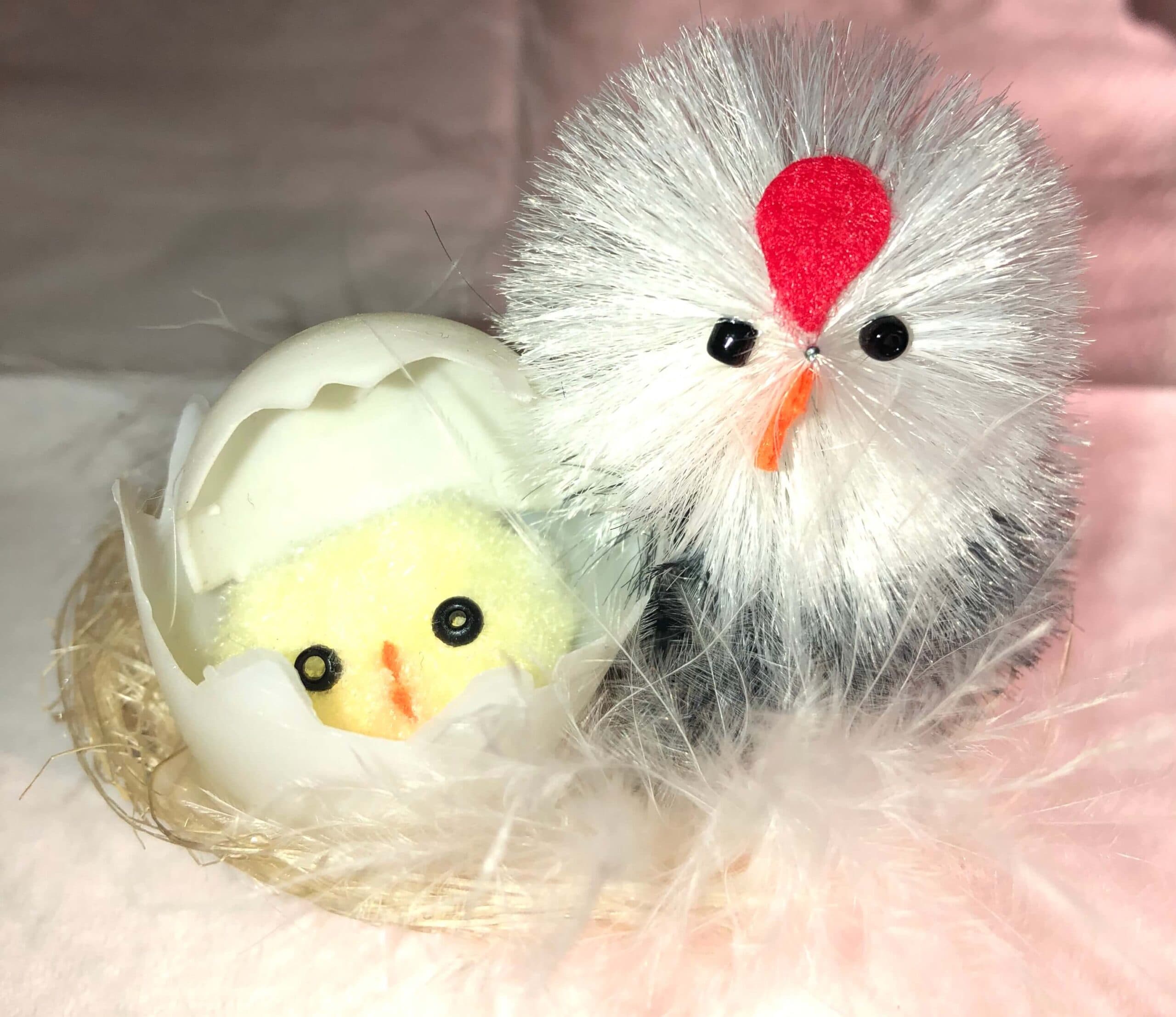 Bílé dekorativní kuřátko a slepička v hnízdě s peřím